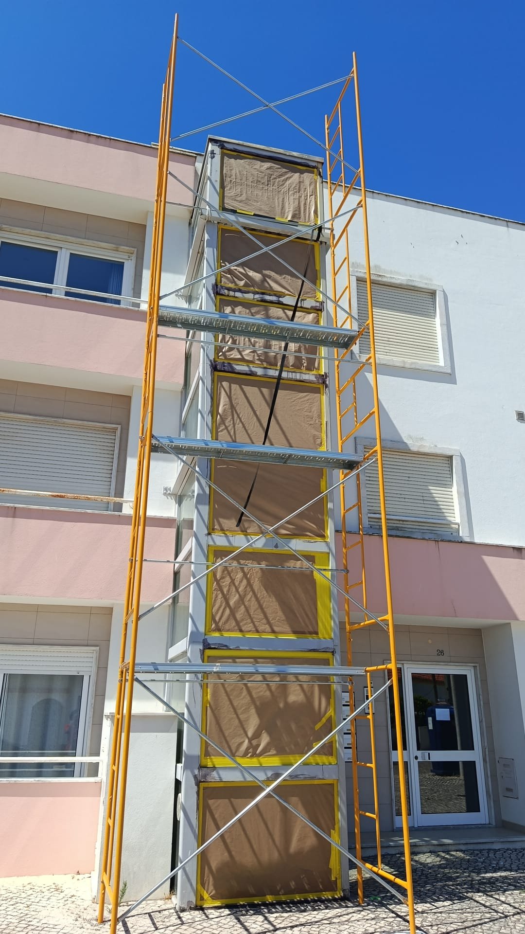Trabalho de pintura exterior numa fachada, com andaime e janelas protegidas